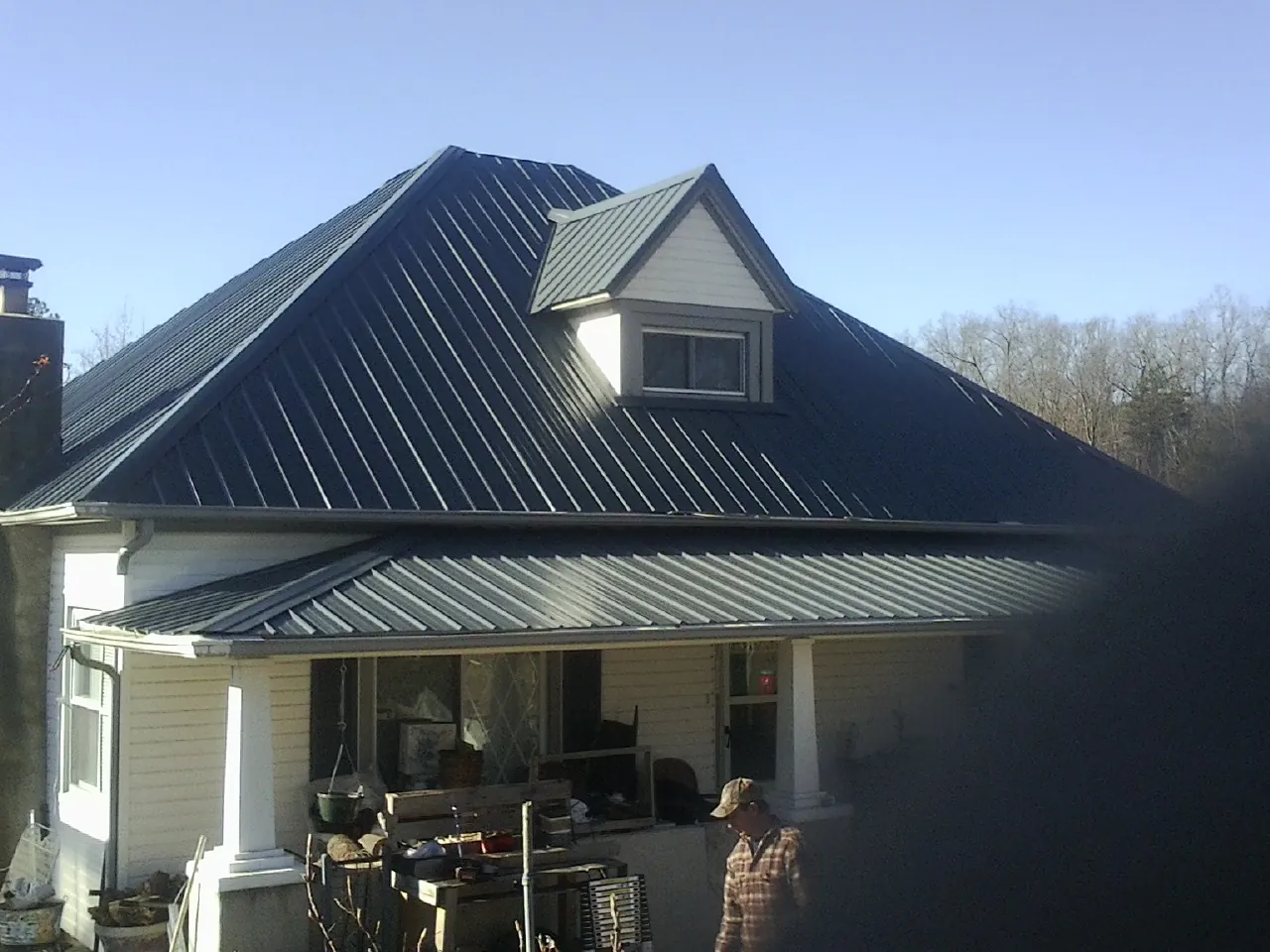 Dark blue standing seam metal roof with a dormer above a front porch in Sparta